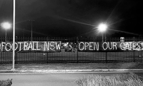 Banner on fence reading: Football NSW Open Our Gates